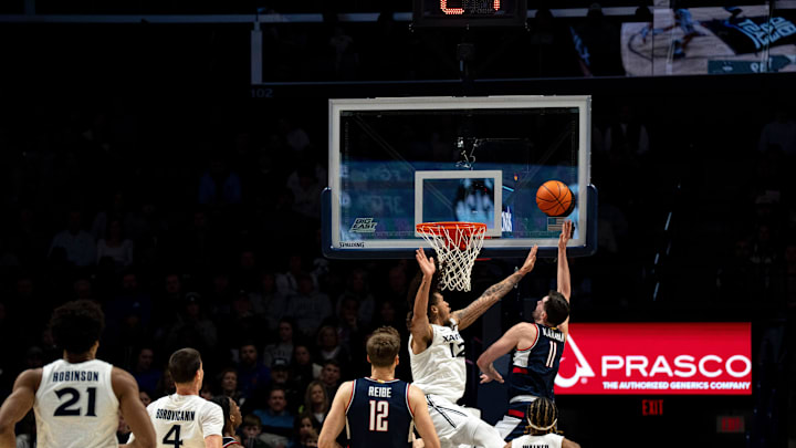 UConn Huskies forward Alex Karaban (11) hits a layup around Xavier Musketeers forward Tre Carroll (12) in the first half of the NCAA basketball game at the Cintas Center in Cincinnati on Dec. 31, 2025.