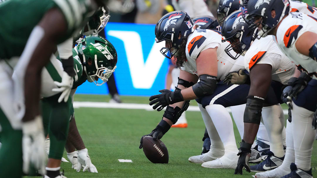 Oct 12, 2025; Tottenham, United Kingdom; Helmets at the line of scrimmage as Denver Broncos center Luke Wattenberg (60) snaps the ball against the New York Jets during an NFL International Series game at Tottenham Hotspur Stadium. Mandatory Credit: Kirby Lee-Imagn Images