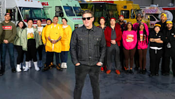 Nishaan, Fat Kid Food Co., Stop Drop N Roll, Rising Tiger, Good Fortune Company, Eat My Biscuits, Burger Walla, G’s Cheesesteaks and Cooking with Que team members in front of their trucks with host Tyler Florence, as seen on The Great Food Truck Race, Season 18.