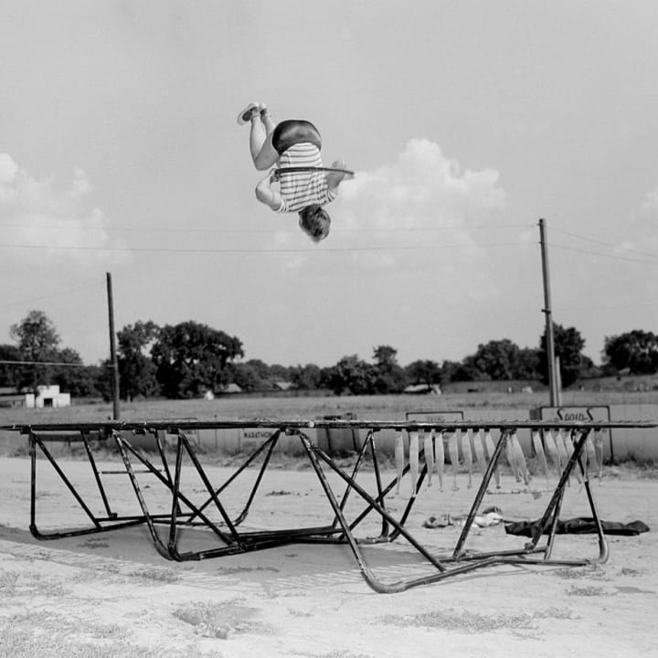 A boy wearing a hula hoop jumps on a trampoline, ca. 1955