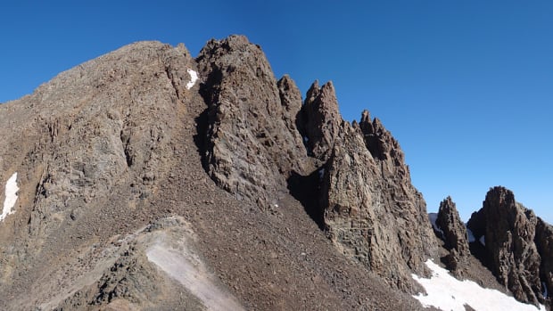 A very steep and rocky mountain with snow at the bottom.