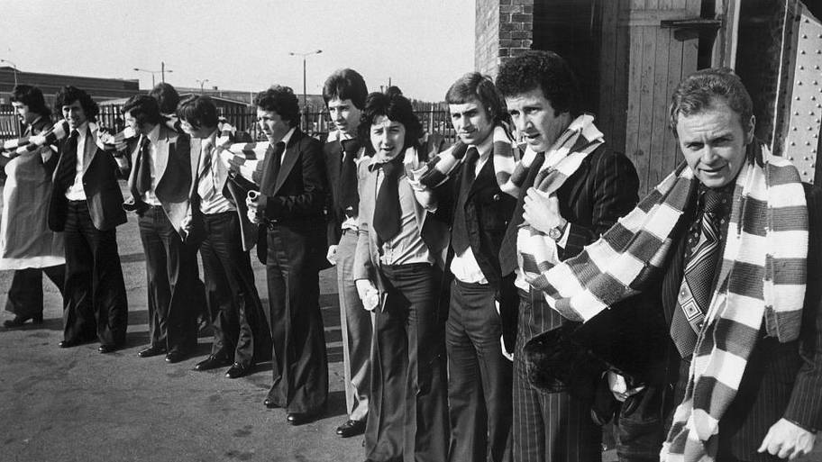 Wrexham football players presented with a 60 foot scarf knitted by a fan before taking off from Liverpool airport.