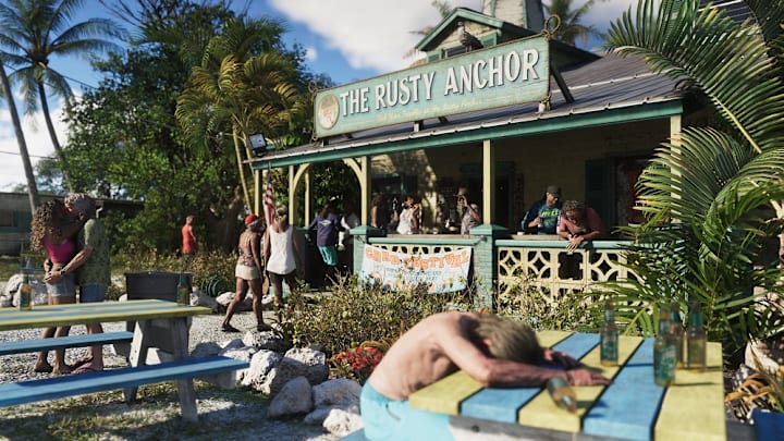 A man is sleeping at a beachfront bar's beer garden as people queue for a drink.