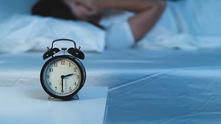 Person in bed with head in hands in the background, with clock in foreground Person in bed with head in hands in the background, with clock in foreground
