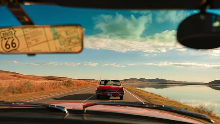 View of a convertible driving in front of a car with Route 66 map in the mirror View of a convertible driving in front of a car with Route 66 map in the mirror