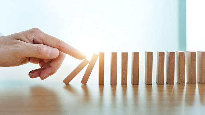 Finger pushing down a domino on wood table