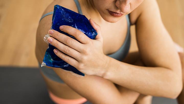 Woman in athletic wear puts ice pack on shoulder