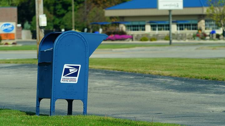 Blue postal mailbox standing beside road and green grass