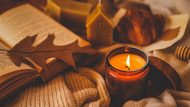 Burning amber candle with an open book, autumn leaf, croissant, and cozy knitted textures. Warm hygge atmosphere for relaxing reading time during the fall season. Burning amber candle with an open book, autumn leaf, croissant, and cozy knitted textures. Warm hygge atmosphere for relaxing reading time during the fall season.