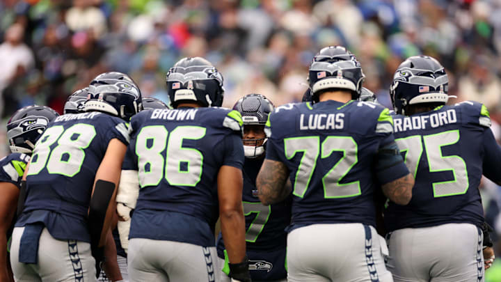 SEATTLE, WASHINGTON - NOVEMBER 24: Geno Smith #7 of the Seattle Seahawks huddles with his teammates AJ Barner #88, Pharaoh Brown #86, Abraham Lucas #72, Anthony Bradford #75 of the Seattle Seahawks during the first quarter against the Arizona Cardinals at Lumen Field on November 24, 2024 in Seattle, Washington.
