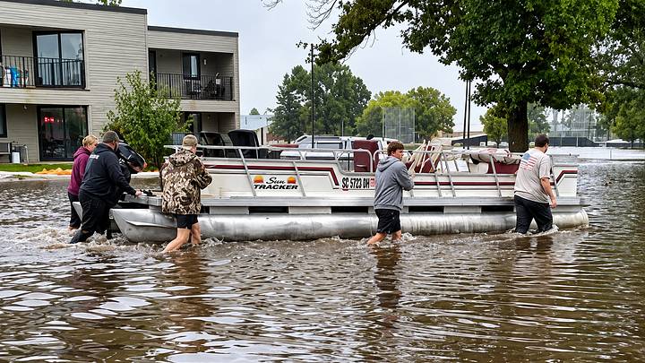 Members of the New Richland-Hartland-Ellendale-Geneva (NRHEG) football team pushed a pontoon boat through flood waters to help evacuate residents from the New Richland Care Center after the Minnesota town was devastated by flood waters on Saturday. Members of the New Richland-Hartland-Ellendale-Geneva (NRHEG) football team pushed a pontoon boat through flood waters to help evacuate residents from the New Richland Care Center after the Minnesota town was devastated by flood waters on Saturday.