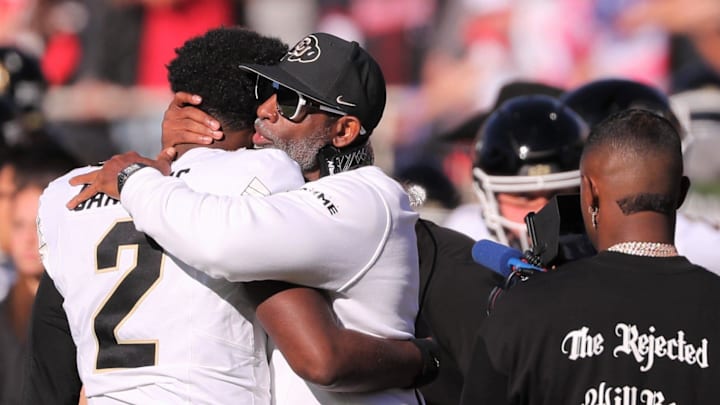 Deion Sanders Sr. embraces his son, Shedeur, while Deion Sanders Jr. (right) videographs 