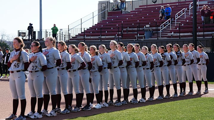 The Virginia Tech Softball team stands in order down the third base line for the national anthem.