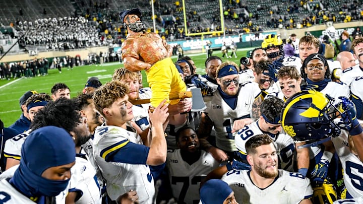 Michigan's J.J. McCarthy holds up the Paul Bunyan trophy as the team celebrates after beating Michigan State