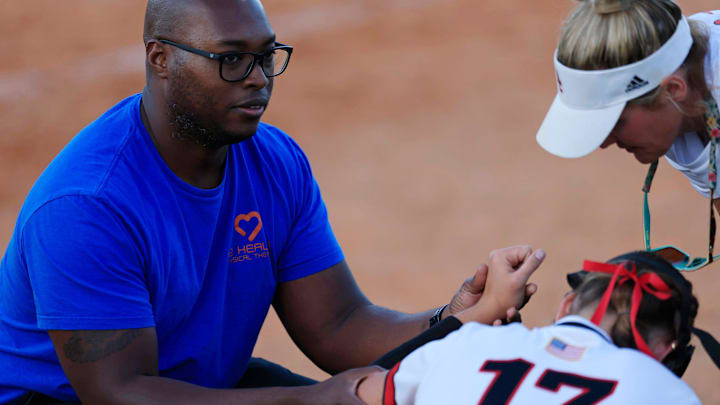 Baker County's Baleigh Shields (17) has her hand checked out by a trainer, left, as Baker County head coach Kylee Canaday leans in during the fifth inning of a regular season high school softball matchup Tuesday, April 23, 2024 at Baker County High School in Glen St. Mary, Fla. The Baker County Wildcats defeated the Middleburg Broncos 6-3.