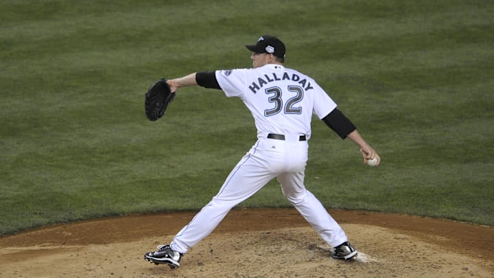 Former Toronto Blue Jays pitcher Roy Halladay throws a pitch wearing a white jersey and black hat.