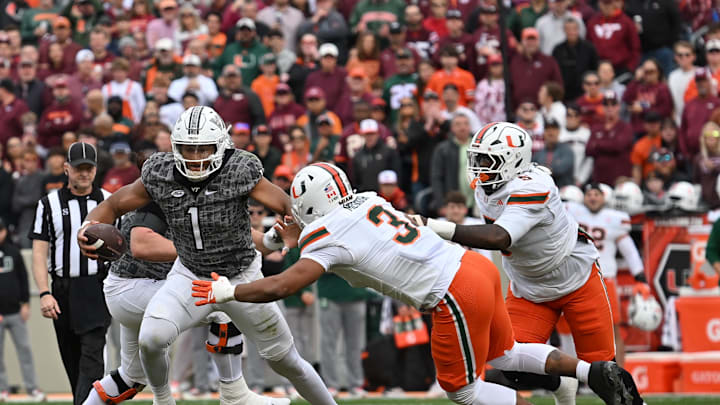 Nov 22, 2025; Blacksburg, Virginia, USA; Virginia Tech Hokies quarterback Kyron Drones (1) breaks a tackle from Miami (FL) Hurricanes defensive lineman Akheem Mesidor (3) during the first quarter at Lane Stadium. Mandatory Credit: Brian Bishop-Imagn Images