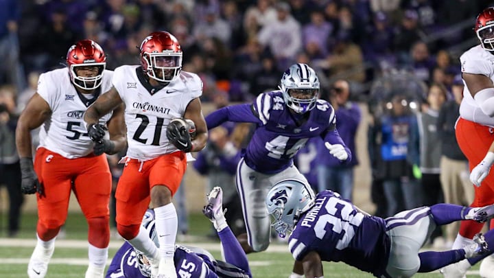 Nov 23, 2024; Manhattan, Kansas, USA; Cincinnati Bearcats running back Corey Kiner (21) runs away from Kansas State Wildcats linebackers Desmond Purnell (32) and Austin Romaine (45) during the second quarter at Bill Snyder Family Football Stadium. Mandatory Credit: Scott Sewell-Imagn Images Nov 23, 2024; Manhattan, Kansas, USA; Cincinnati Bearcats running back Corey Kiner (21) runs away from Kansas State Wildcats linebackers Desmond Purnell (32) and Austin Romaine (45) during the second quarter at Bill Snyder Family Football Stadium. Mandatory Credit: Scott Sewell-Imagn Images