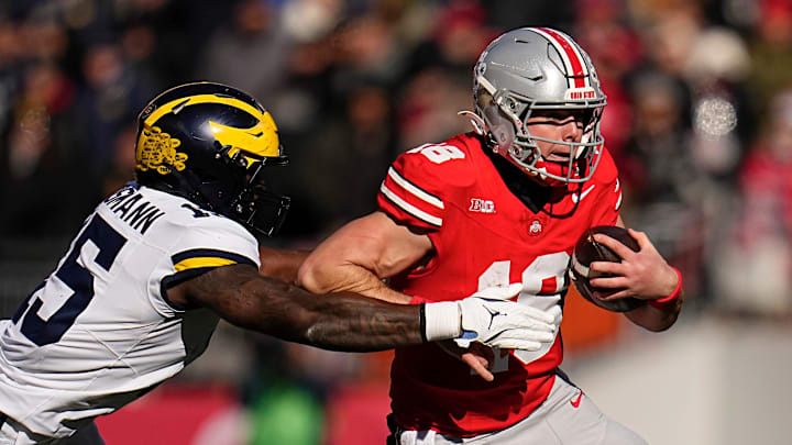 Ohio State Buckeyes quarterback Will Howard (18) runs past Michigan Wolverines linebacker Ernest Hausmann (15) during the NCAA football game at Ohio Stadium in Columbus on Tuesday, Dec. 3, 2024. Michigan won 13-10.