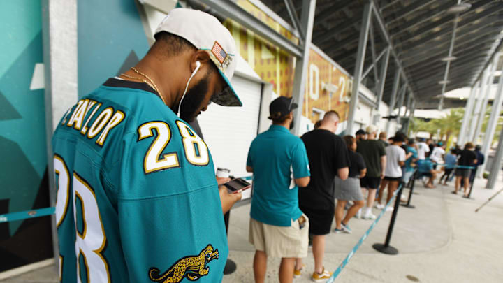Jonathan Breaker looks at his phone, waiting for the online drop of the new Jaguars throwback jerseys as he waits in line for the Pro Shop wearing an original vintage Fred Taylor jersey Thursday morning. The Jacksonville Jaguars unveiled the team's new throwback jerseys Thursday morning, July 18, 2024 during a reveal at the Miller Electric Center near EverBank Stadium. Fans lined up down the street for the opportunity to purchase throwback Trevor Lawrence and Travis Etienne Jr. jerseys as well