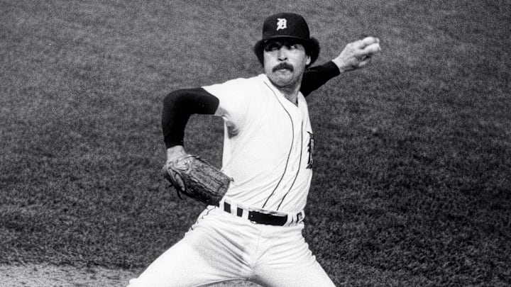 Former Detroit Tigers pitcher Willie Hernandez throws a pitch wearing a white jersey and navy blue hat.