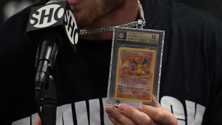 Jun 6, 2021; Miami, Florida, USA; Logan Paul holds up a Pokemon Charizard card he wears around his neck while speaking to the media after his fight against Floyd Mayweather Jr. (not pictured) at Hard Rock Stadium. Mandatory Credit: Jasen Vinlove-Imagn Images Jun 6, 2021; Miami, Florida, USA; Logan Paul holds up a Pokemon Charizard card he wears around his neck while speaking to the media after his fight against Floyd Mayweather Jr. (not pictured) at Hard Rock Stadium. Mandatory Credit: Jasen Vinlove-Imagn Images