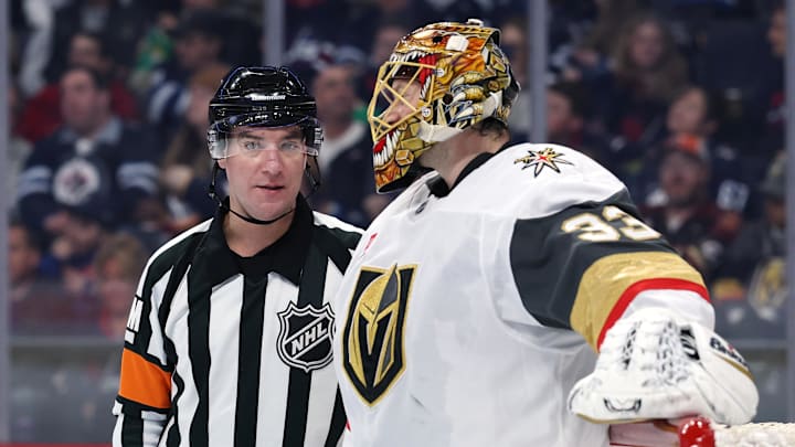 Mar 24, 2026; Winnipeg, Manitoba, CAN; Referee Pierre Lambert (25) talks with Vegas Golden Knights goaltender Adin Hill (33) during break in play against the Winnipeg Jets in the second period at Canada Life Centre. Mandatory Credit: James Carey Lauder-Imagn Images