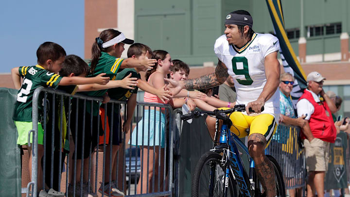 Green Bay Packers wide receiver Christian Watson (9) greets fans while riding a fan's bicycle along the DreamDrive before the start of training camp on Aug. 3, 2023, in Green Bay, Wis.
