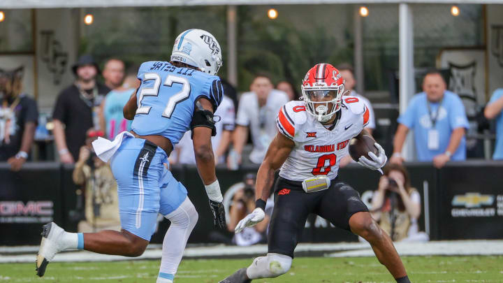 Nov 11, 2023; Orlando, Florida, USA; Oklahoma State Cowboys running back Ollie Gordon II (0) runs the ball in front of UCF Knights linebacker Walter Yates III (27) during the first quarter at FBC Mortgage Stadium. Mandatory Credit: Mike Watters-USA TODAY Sports