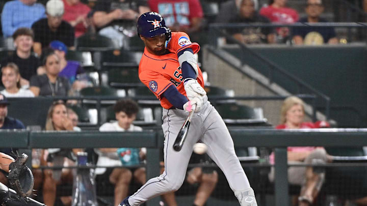 A baseball player in white pants and an orange jersey swinging a black baseball bat toward a ball