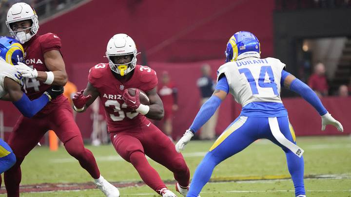 Arizona Cardinals running back Trey Benson (33) runs through a hole against Los Angeles Rams cornerback Cobie Durant (14) during the second quarter at State Farm Stadium. Arizona Cardinals running back Trey Benson (33) runs through a hole against Los Angeles Rams cornerback Cobie Durant (14) during the second quarter at State Farm Stadium.