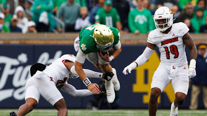 Notre Dame quarterback Riley Leonard, center, flies through the air while being tackled during a NCAA college football game between Notre Dame and Louisville at Notre Dame Stadium on Saturday, Sept. 28, 2024, in South Bend.
