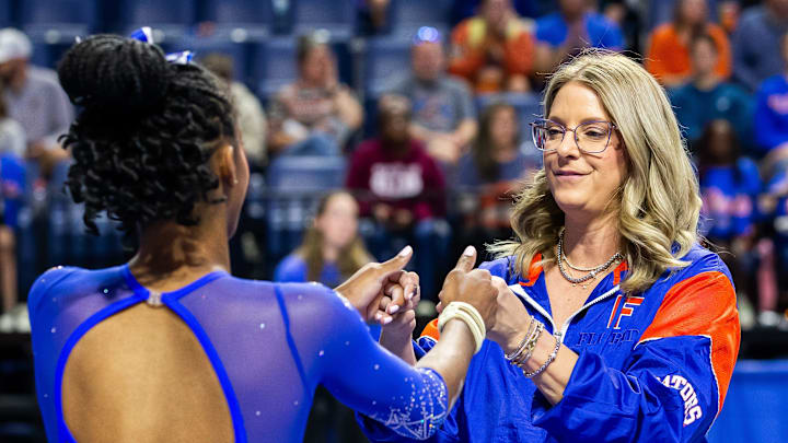 Coach Jenny Rowland give fist bumps to Anaya Pilgrim before her balance beam routine.  [Doug Engle/Gainesville Sun]