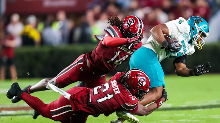 Nov 22, 2025; Columbia, South Carolina, USA; Coastal Carolina Chanticleers running back Jalen John (21) is brought down by South Carolina Gamecocks defensive back Kelvin Hunter (21) and linebacker Jaron Willis (14) in the second half at Williams-Brice Stadium. Mandatory Credit: Jeff Blake-Imagn Images