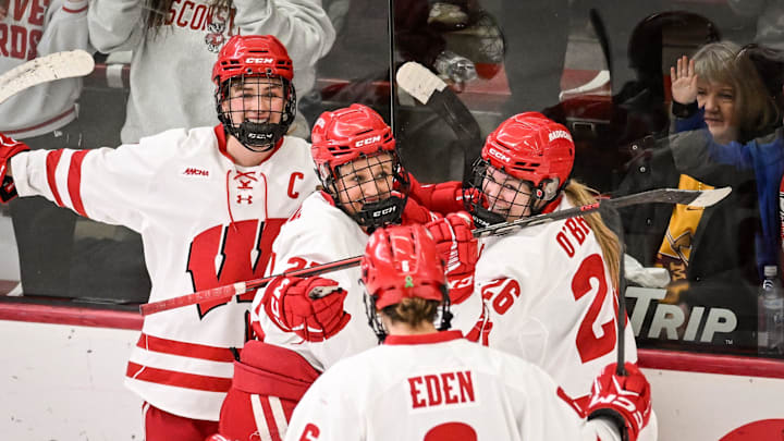 Teammates mob Wisconsin Badgers left wing Kirsten Simms (27) after her goal against the Minnesota Gophers in the second period of a game Sunday, February 9, 2025, at LaBahn Arena in Madison, Wisconsin.