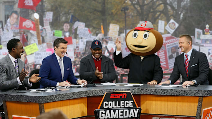 Lee Corso waves while wearing a Brutus Buckeye head as, from left, Desmond Howard, Rece Davis, Archie Griffin, and Kirk Herbstreit applaud his pick during ESPN's College GameDay broadcast from the campus of Ohio State prior to the NCAA football game against the Michigan State Spartans in Columbus on Nov. 21, 2015.