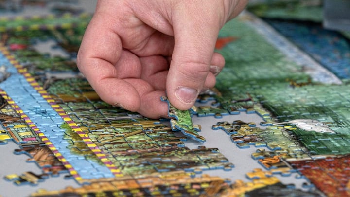 John Walczak places a puzzle piece in place as he shows some of his huge collection of jigsaw puzzles Friday, May 3, 2024 in his Carmel home. He recently achieved a Guinness World Record for the largest collection of jigsaw puzzles.