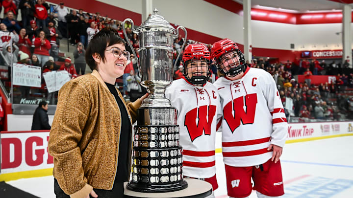 Wisconsin Badgers forward Casey O'Brien (26, center) and defender Caroline Harvey (4) accept the WCHA regular season trophy from commissioner Michelle McAteer after in a game against the Minnesota Gophers on Saturday, February 8, 2025, at LaBahn Arena in Madison, Wisconsin. Wisconsin won, 8-2.