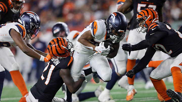 Dec 28, 2024; Cincinnati, Ohio, USA;  Denver Broncos running back Jaleel McLaughlin (38) runs for a first down as Cincinnati Bengals cornerback Mike Hilton (21) and Cincinnati Bengals safety Geno Stone (22) make the tackle during the fourth quarter at Paycor Stadium. Mandatory Credit: Joseph Maiorana-Imagn Images