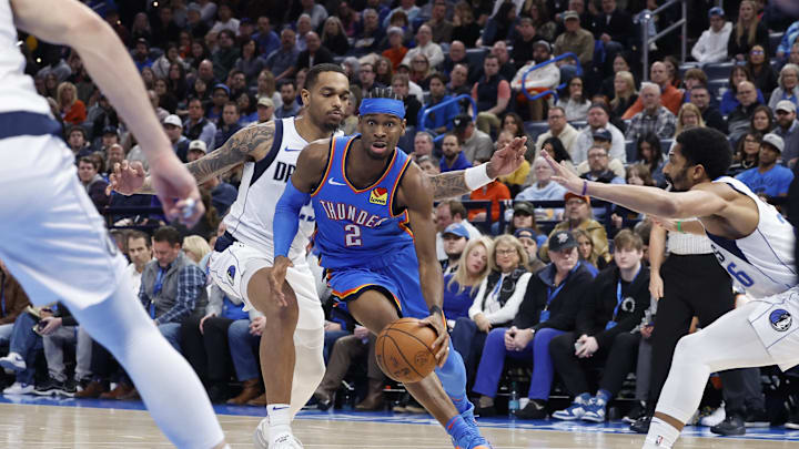 Jan 23, 2025; Oklahoma City, Oklahoma, USA; Oklahoma City Thunder guard Shai Gilgeous-Alexander (2) drives between Dallas Mavericks forward P.J. Washington (25) and guard Spencer Dinwiddie (26) during the second half at Paycom Center. Mandatory Credit: Alonzo Adams-Imagn Images
