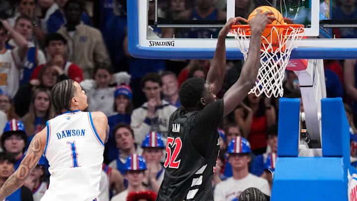 Feb 21, 2026; Lawrence, Kansas, USA; Cincinnati Bearcats center Moustapha Thiam (52) dunks the ball as Kansas Jayhawks guard Jayden Dawson (1) looks on during the second half of the game at Allen Fieldhouse. Mandatory Credit: Denny Medley-Imagn Images