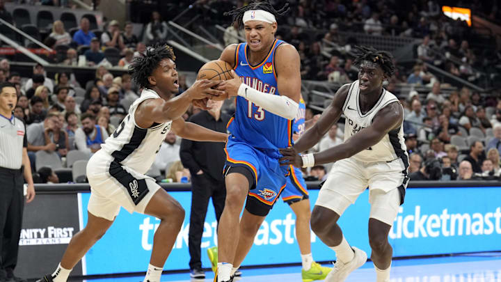 Oct 7, 2024; San Antonio, Texas, USA; Oklahoma City Thunder forward Ousmane Dieng (13) drives to the basket between San Antonio Spurs forward Harrison Ingram (55) and guard Sidy Cissoko (25) during the second half at Frost Bank Center. Mandatory Credit: Scott Wachter-Imagn Images