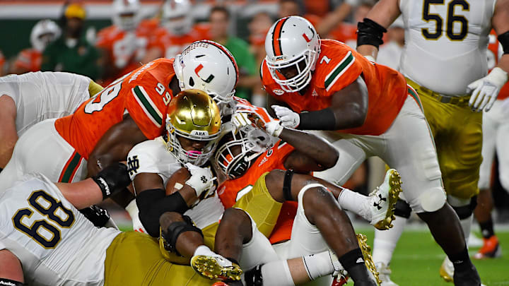Nov 11, 2017; Miami Gardens, FL, USA; Miami Hurricanes defensive lineman Chad Thomas (9) and defensive lineman Joe Jackson (99) and defensive lineman Kendrick Norton (7) bring down Notre Dame Fighting Irish running back Josh Adams (33) during the first half at Hard Rock Stadium. Mandatory Credit: Jasen Vinlove-Imagn Images