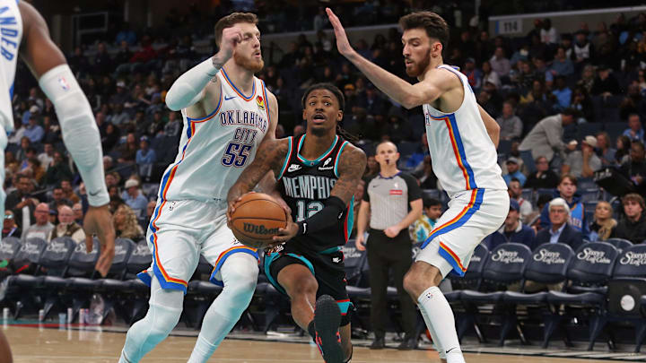 Nov 9, 2025; Memphis, Tennessee, USA; Memphis Grizzlies guard Ja Morant (12) drives to the basket between Oklahoma City Thunder center Isaiah Hartenstein (55) and center Chet Holmgren (7) during the third quarter  at FedExForum. Mandatory Credit: Petre Thomas-Imagn Images