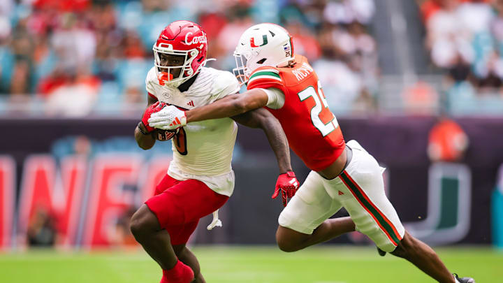 Nov 18, 2023; Miami Gardens, Florida, USA; Louisville Cardinals wide receiver Chris Bell (0) breaks a tackle attempt from Miami Hurricanes defensive back Jadais Richard (25) during the second quarter at Hard Rock Stadium. Mandatory Credit: Sam Navarro-Imagn Images