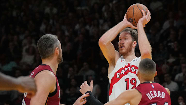Nov 29, 2024; Miami, Florida, USA;  Toronto Raptors center Jakob Poeltl (19) looks the pass the ball as Miami Heat guard Tyler Herro (14) and forward Kevin Love (42) close in during the first half in an NBA Cup game at Kaseya Center. Mandatory Credit: Jim Rassol-Imagn Images