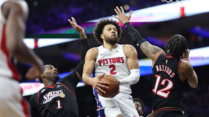 Nov 9, 2025; Philadelphia, Pennsylvania, USA; Detroit Pistons guard Cade Cunningham (2) drives for a shot between Philadelphia 76ers forward Trendon Watford (12) and center Andre Drummond (1) during the first quarter at Xfinity Mobile Arena. Mandatory Credit: Bill Streicher-Imagn Images