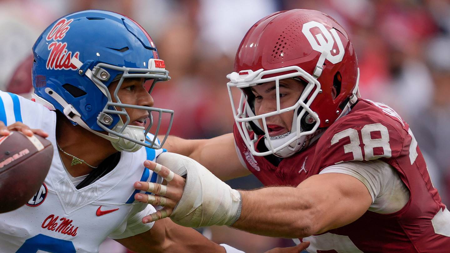 Un quarterback di college in azione durante un match, con un team dietro di lui, in un campo di calcio