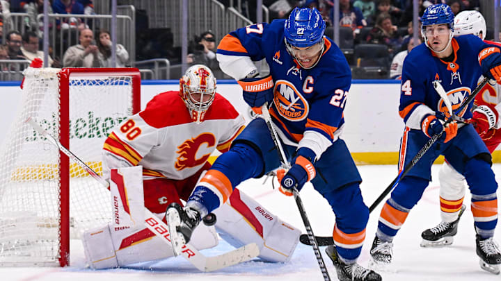 Mar 22, 2025; Elmont, New York, USA;  New York Islanders left wing Anders Lee (27) attempts to deflect the puck in front of Calgary Flames goaltender Dan Vladar (80) during the second period at UBS Arena. Mandatory Credit: Dennis Schneidler-Imagn Images