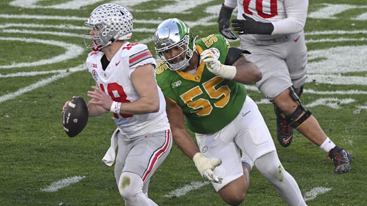 Jan 1, 2025; Pasadena, CA, USA;  Ohio State Buckeyes quarterback Will Howard (18) looks for an open receiver as Oregon Ducks defensive lineman Derrick Harmon (55) closes in durigt the third quarter at Rose Bowl Stadium. Mandatory Credit: Robert Hanashiro-Imagn Images